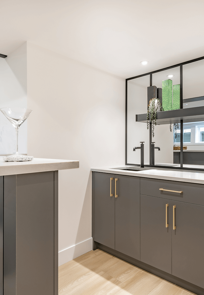 Modern basement wet bar with graphite cabinetry, brass hardware and a black-framed mirror wall