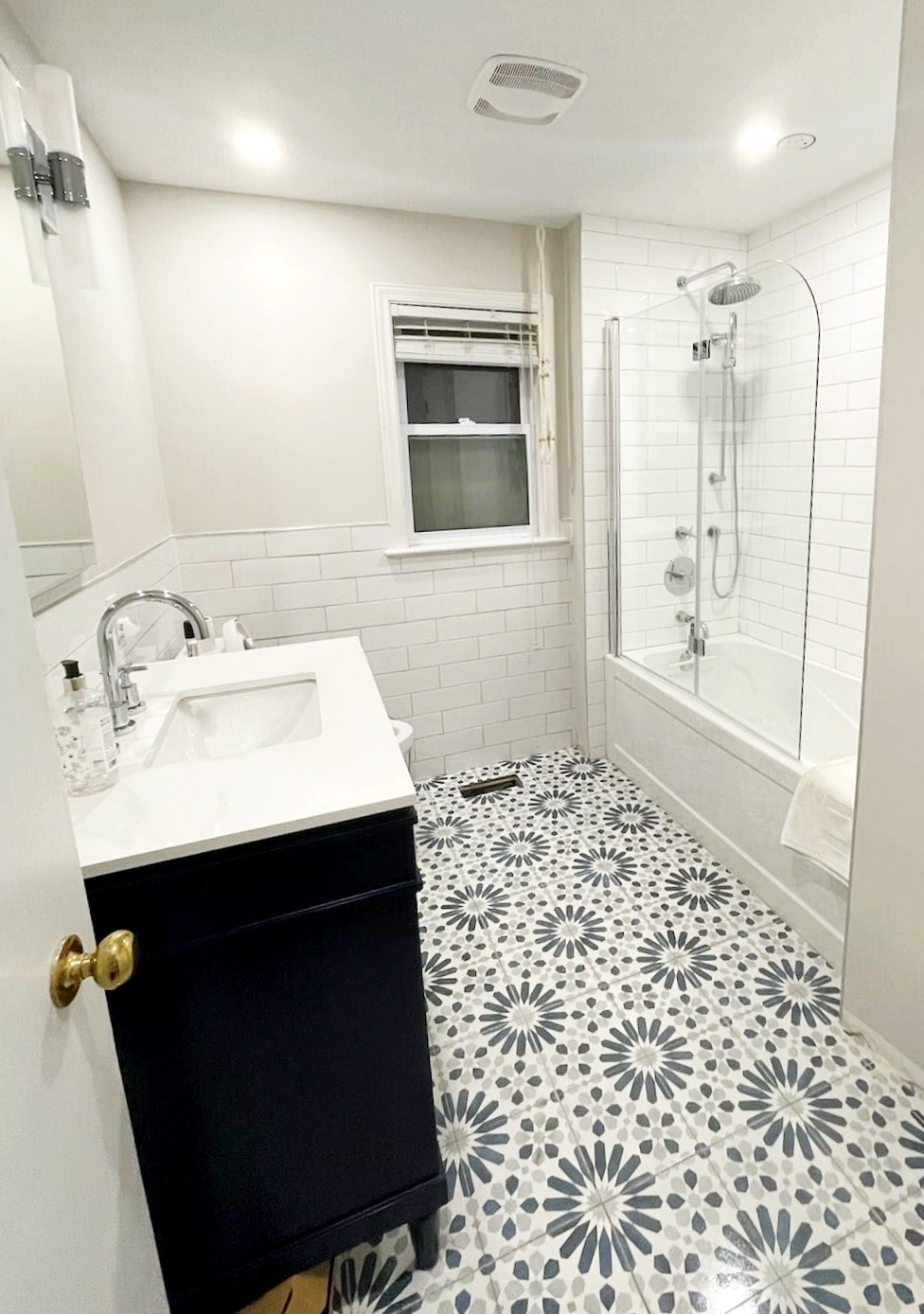 Renovated bathroom with patterned encaustic floor tile, subway tile and a navy vanity